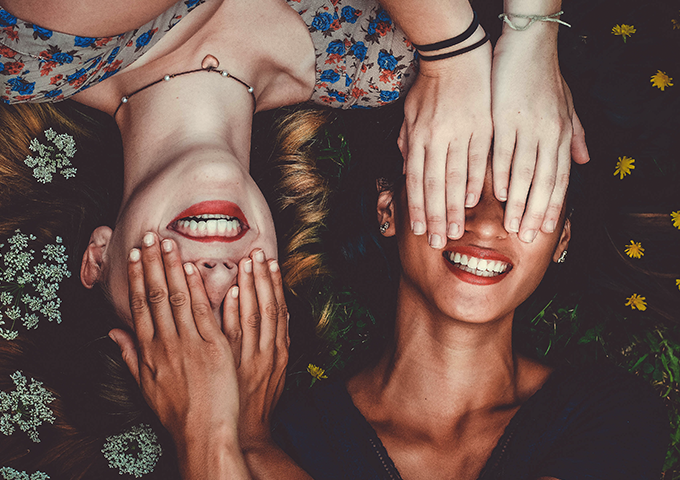 Two women on the ground, covering each other's eyes and laughing.