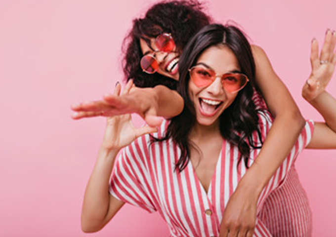 Two women in pink sunglasses laughing and being playful.